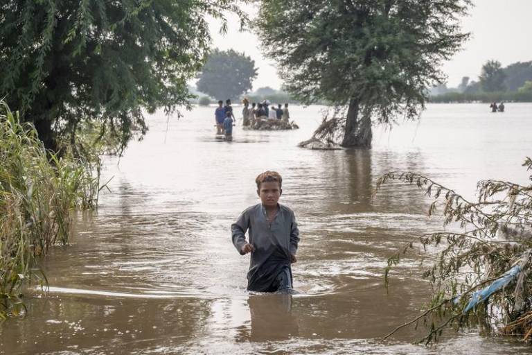 Un niño de siete años se abre paso a través de aguas de inundación hasta la altura de la cintura en Punjab, Pakistán, en septiembre de 2025.