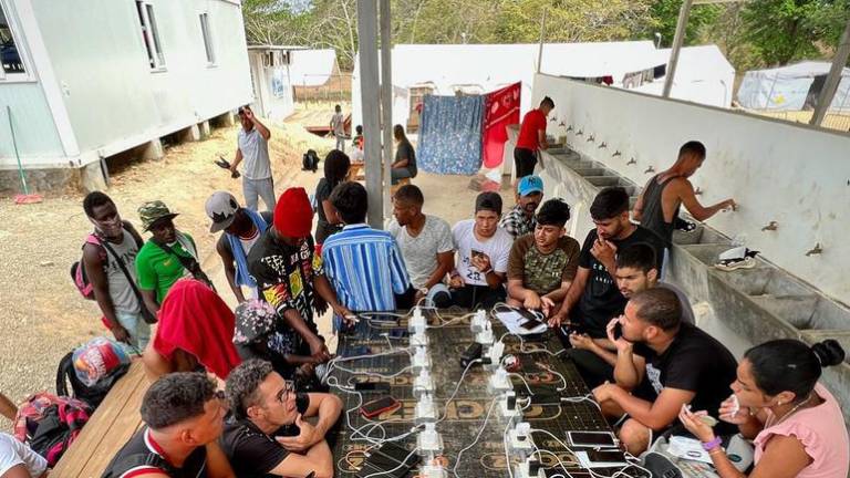 Migrantes y refugiados cargando sus teléfonos en un enchufe de la Estación de Acogida de Migrantes tras cruzar la selva del Darién.