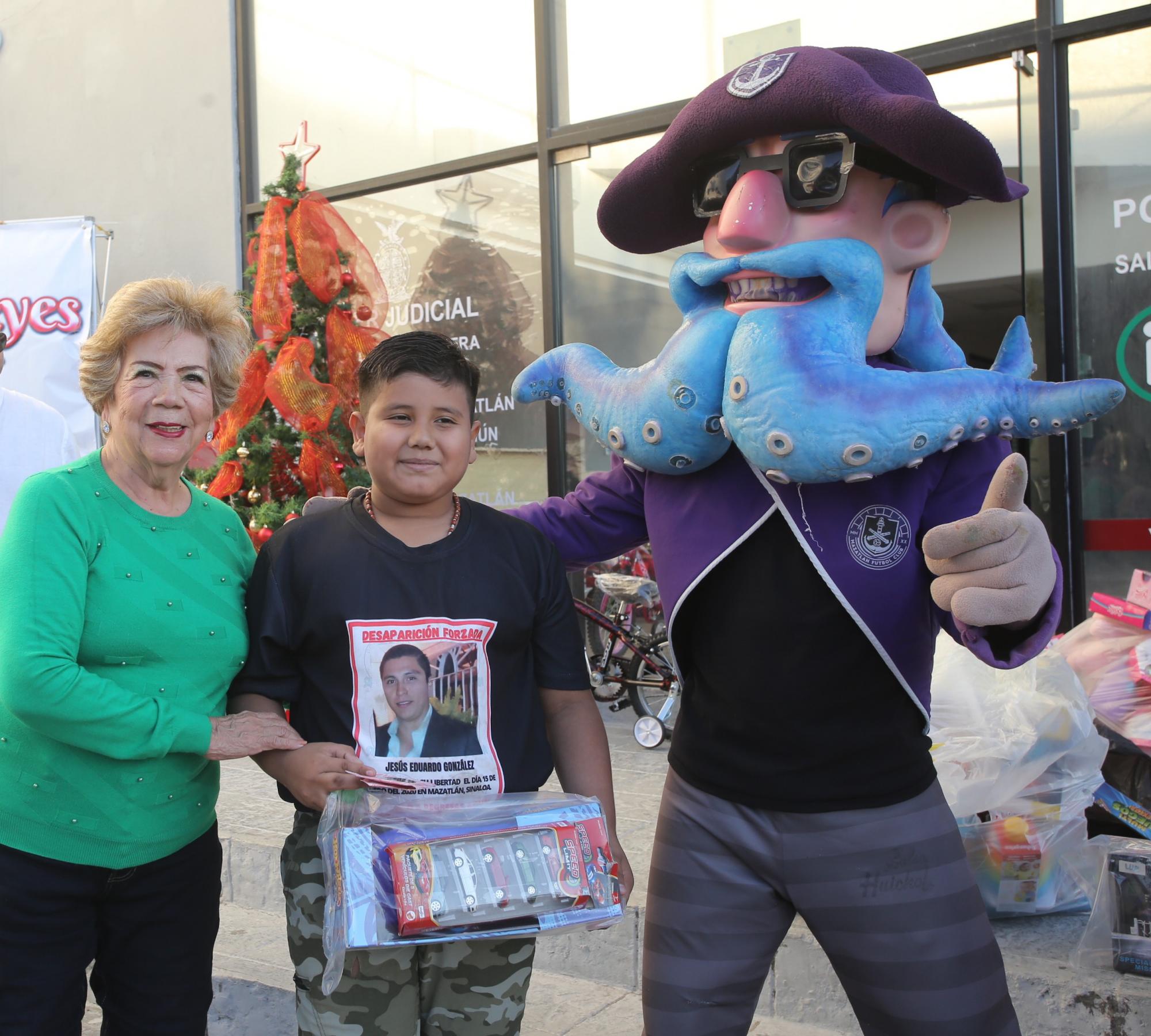 $!Lucy Calleros de Soto, responsable del área de espiritualidad y moral de la Unidad Datemex de Anspac Mazatlán, hace entrega de un obsequio a Sergio Alejandro, quien quiere ser sacerdote, aquí junto a el Capitán Krak.