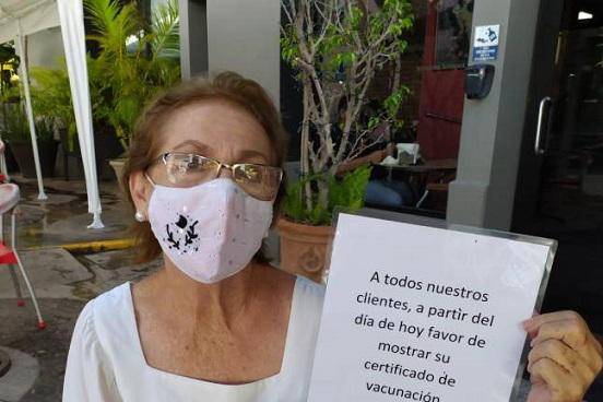 La dueña de un comercio en Mazatlán muestra lo que colocó en su negocio para informar a los clientes que debían presentar el certificado de vacunación para ingresar.