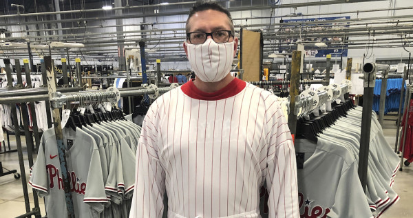 Una persona muestra una bata y una mascarilla hecha con la tela originalmente destinada para producir un uniforme de los Filis de Filadelfia.