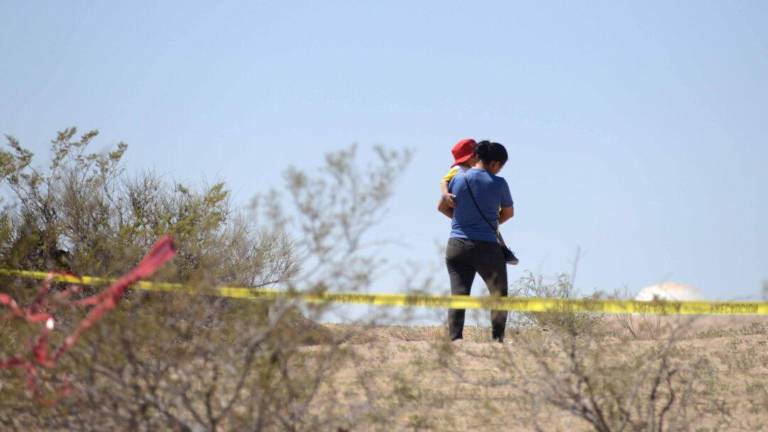 Una mujer con un niños en brazos camina sobre el terreno baldío donde se localizaron fosas clandestinas en Ciudad Juárez, en septiembre de 2023.