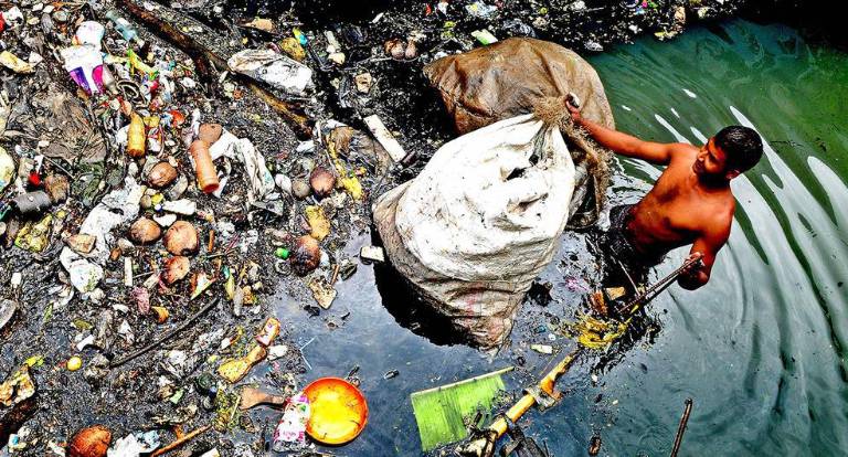 Un recogedor de basura se sumerge hasta la cintura en el agua de un canal de Kochi (India).