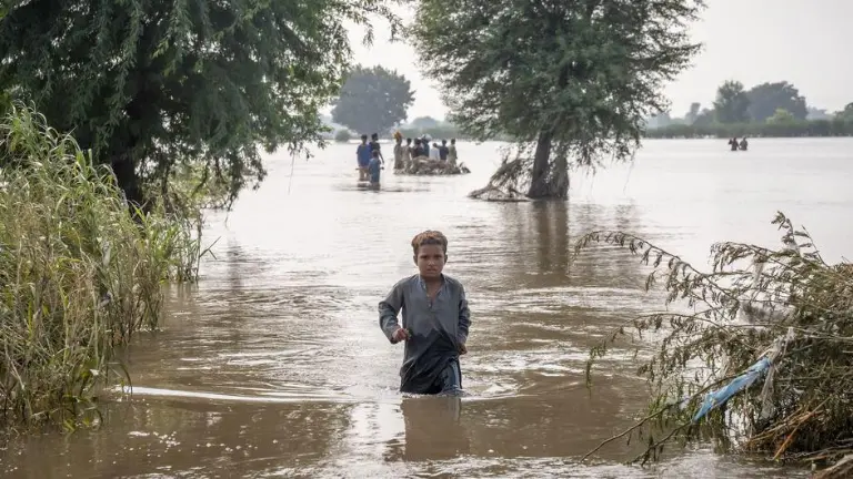 Un niño de siete años se abre paso a través de aguas de inundación hasta la altura de la cintura en Punjab, Pakistán, en septiembre de 2025.
